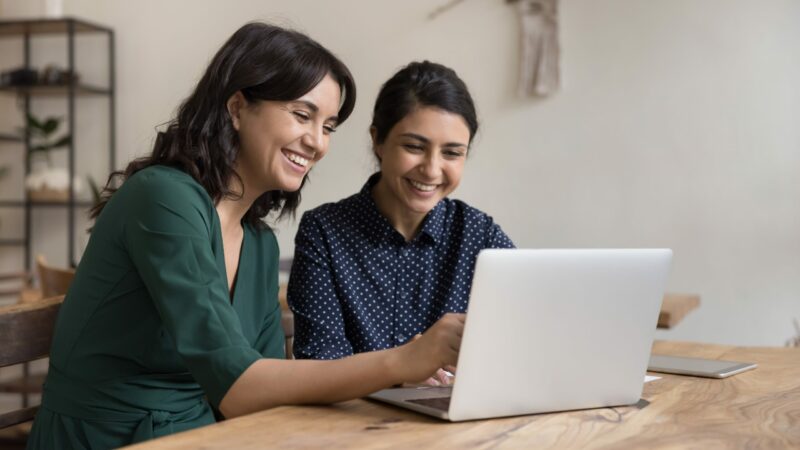 Two,Cheerful,Diverse,Office,Workers,Women,Cooperating,On,Project,,Sitting